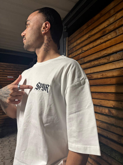 Man wearing a white t-shirt with 'SPYR' logo against a wooden wall.