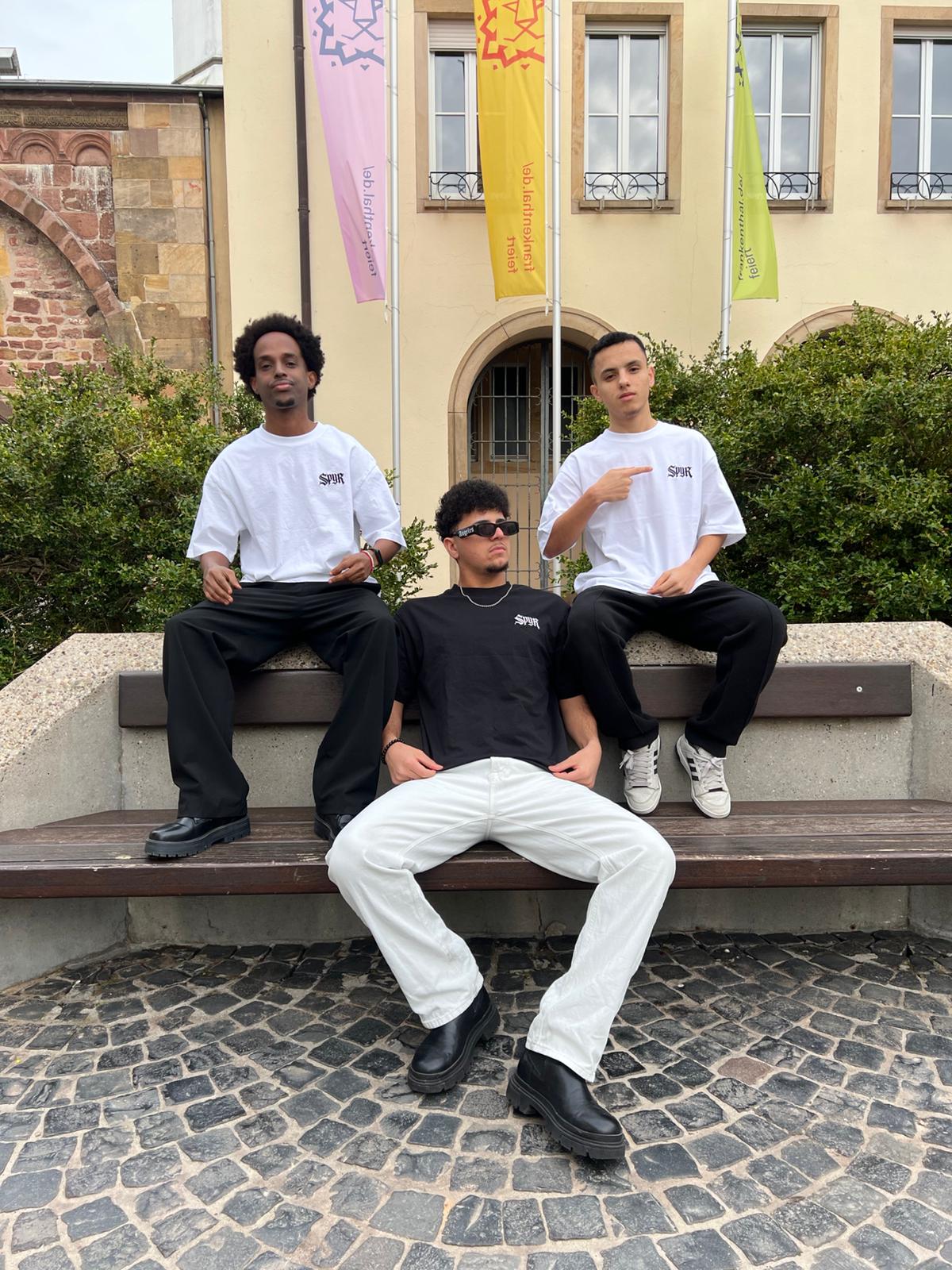 Three individuals sitting on a bench in front of a building with flags